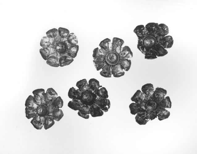 Golden laurel (?) rosette with eight petals.  Rosette has a central boss at the base.  The sleeve of each boss protrudes through the rear of the rosette.  On the rear are two tube eyelets.  Each petal curves concavely.
Condition:  Several petals and stamens bent; one eyelet missing; dirty.