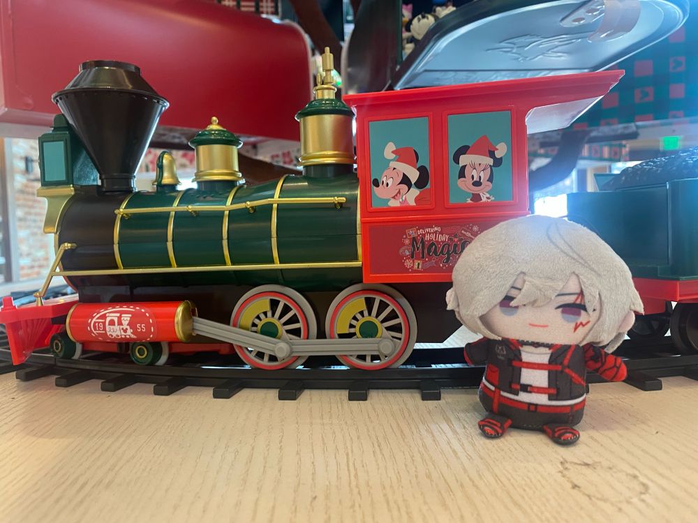 Fulgur Ovid plush sitting with a toy train with Mickey and Minnie Mouse. 