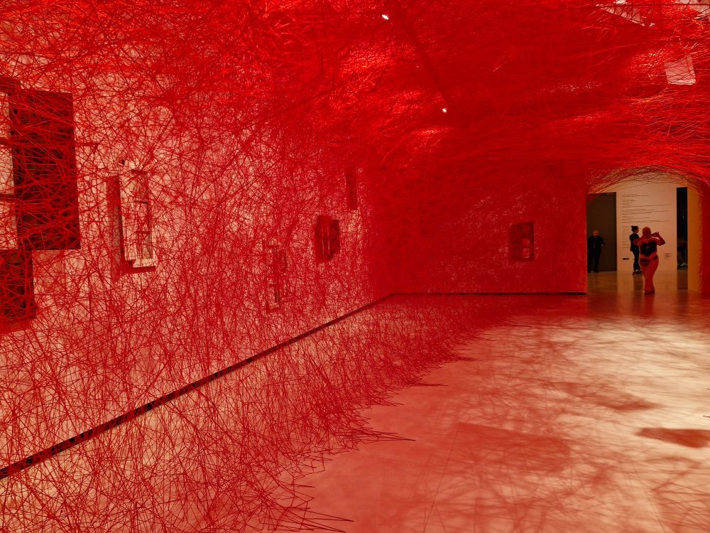 red threads woven through the space in a gallery creating a tunnel-like effect