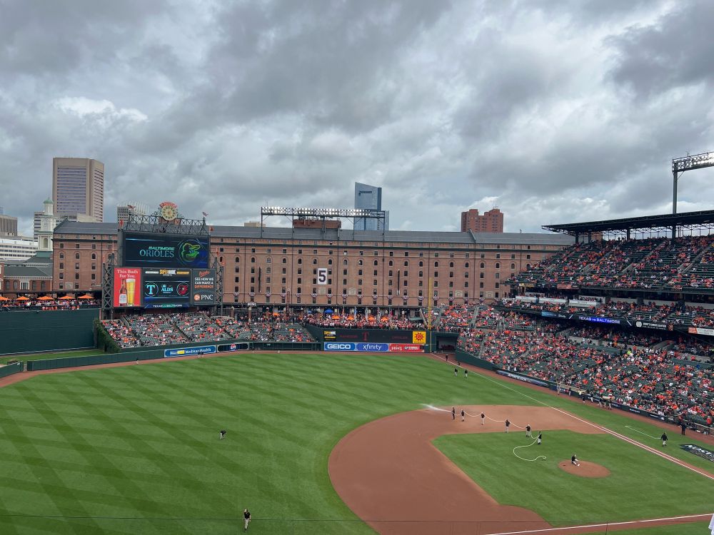 A view of Camden Yards from upper deck seats behind the third base line. Grounds crew workers are spraying water on the infield dirt.