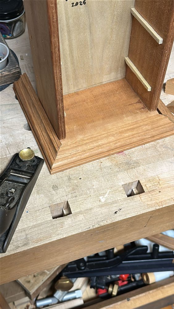 A worn block plane next to the base of the tiny mahogany cabinet, with the mitred molding place against it 