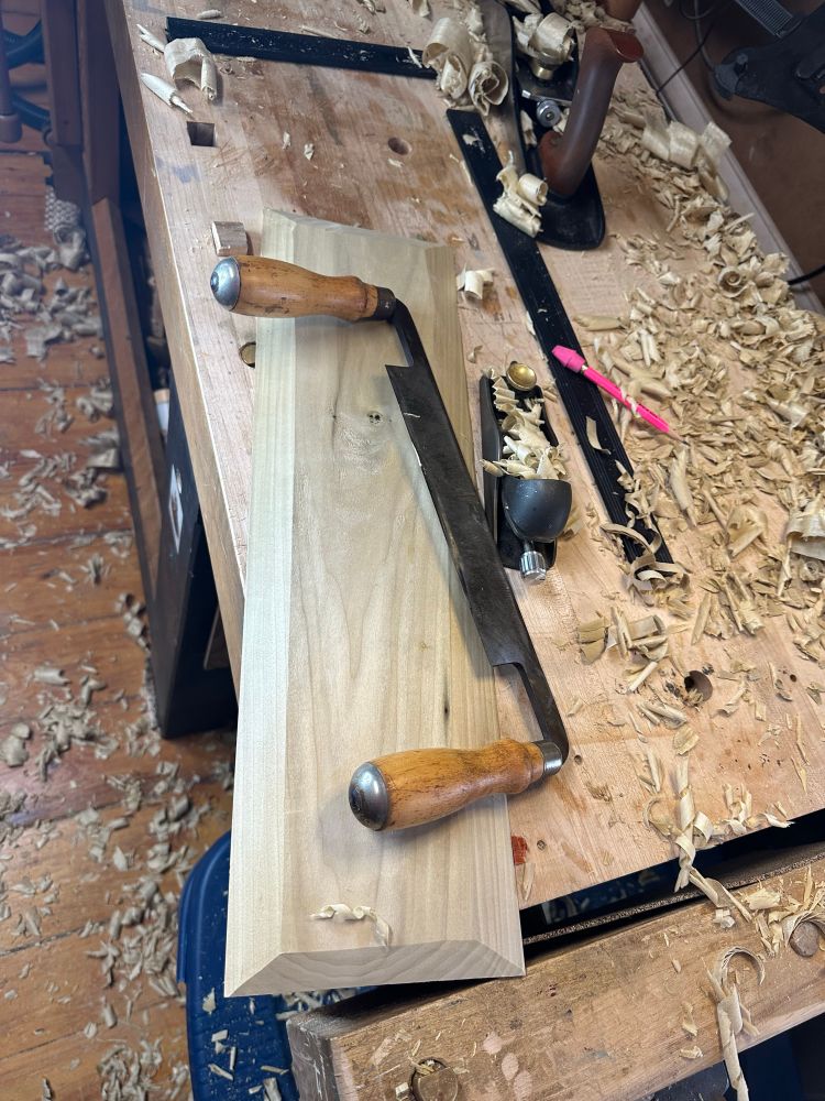A drawknife and block plane sitting on the back panel before installation, surrounded by shavings from the scrub plane and other tools.  