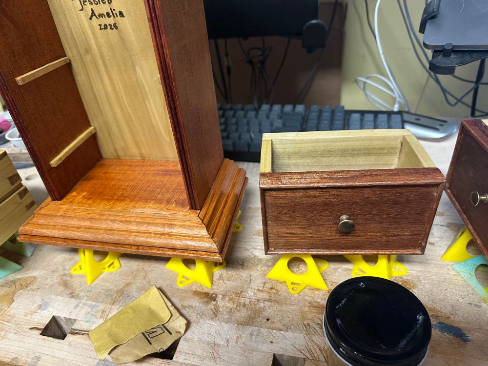 A closeup of one of the drawer fronts, made of mahogany and poplar with applied cockbeading, and the base of the cabinet with a complex molding and drawer runners inside.  The poplar back has a signature and year on it. 