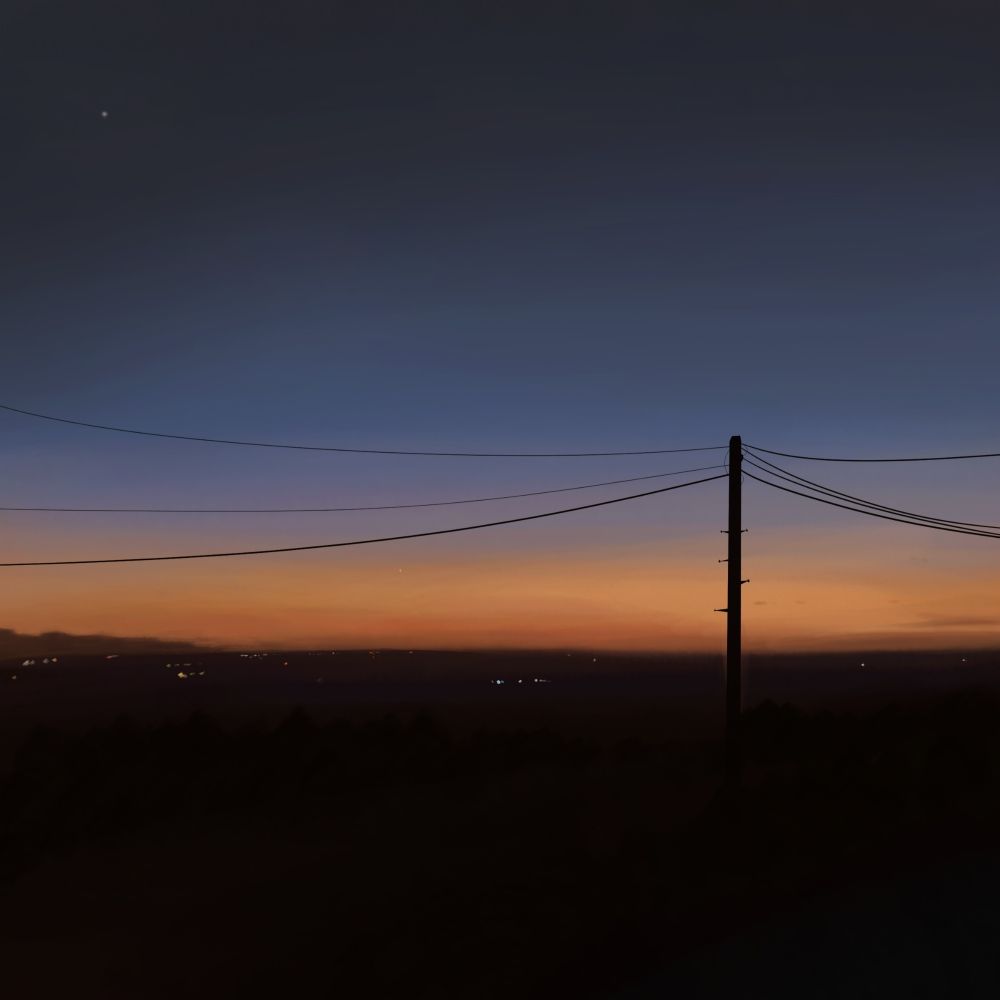 A late sunset, a silhouette of a telephone pole is in the foreground, some city lights are visible.