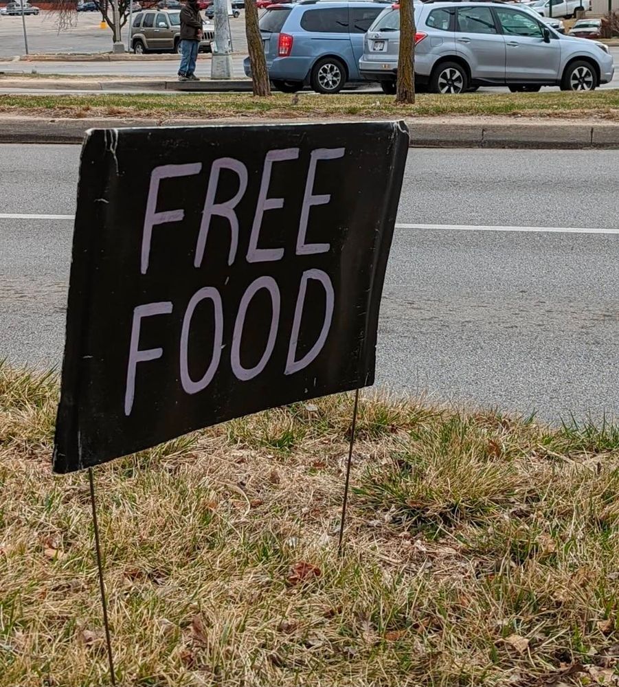 Black sign with words "FREE FOOD" on it next to a road.