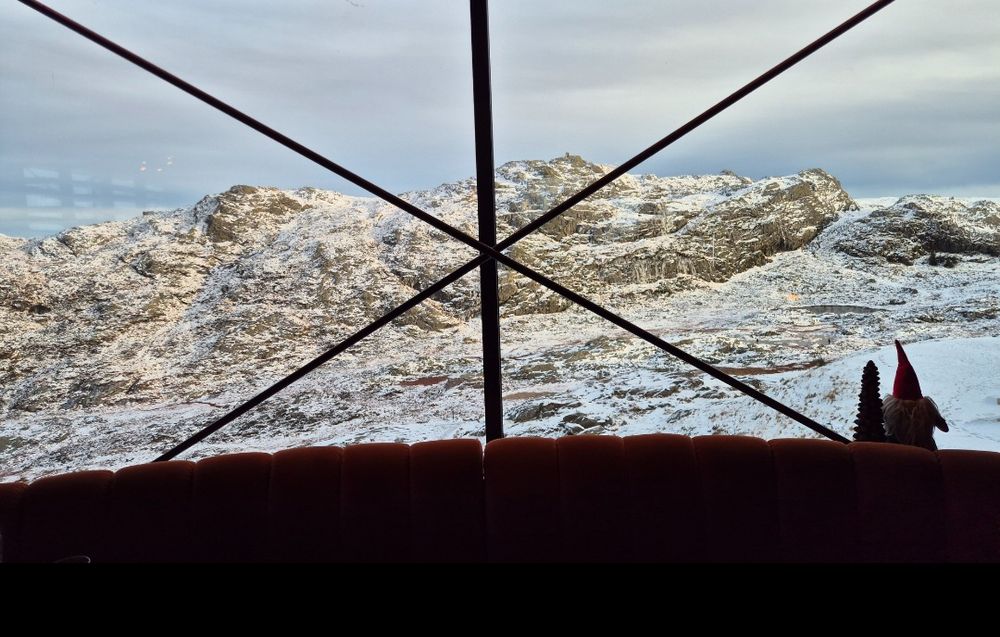 This picture captures a scenic view of snow-covered mountains through a large window with a cross-frame structure. 