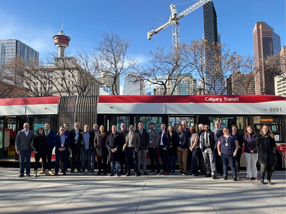  A group of people standing in front of an extended bus with a cityscape behind it