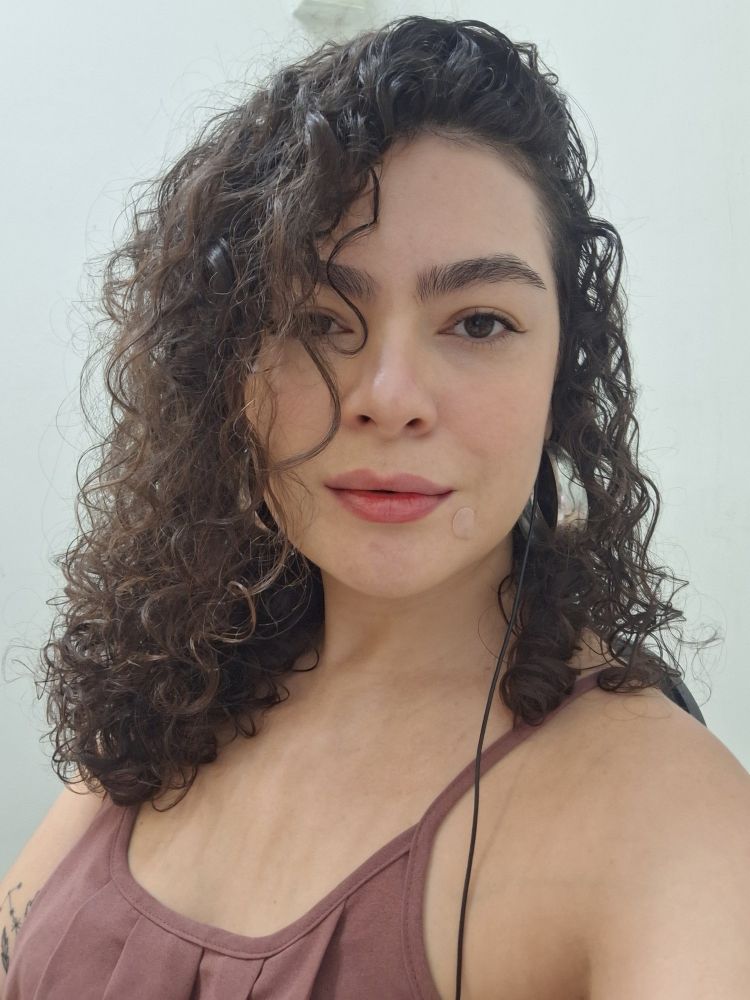 Selfie de mulher branca de cabelo castanho cacheado abaixo dos ombros