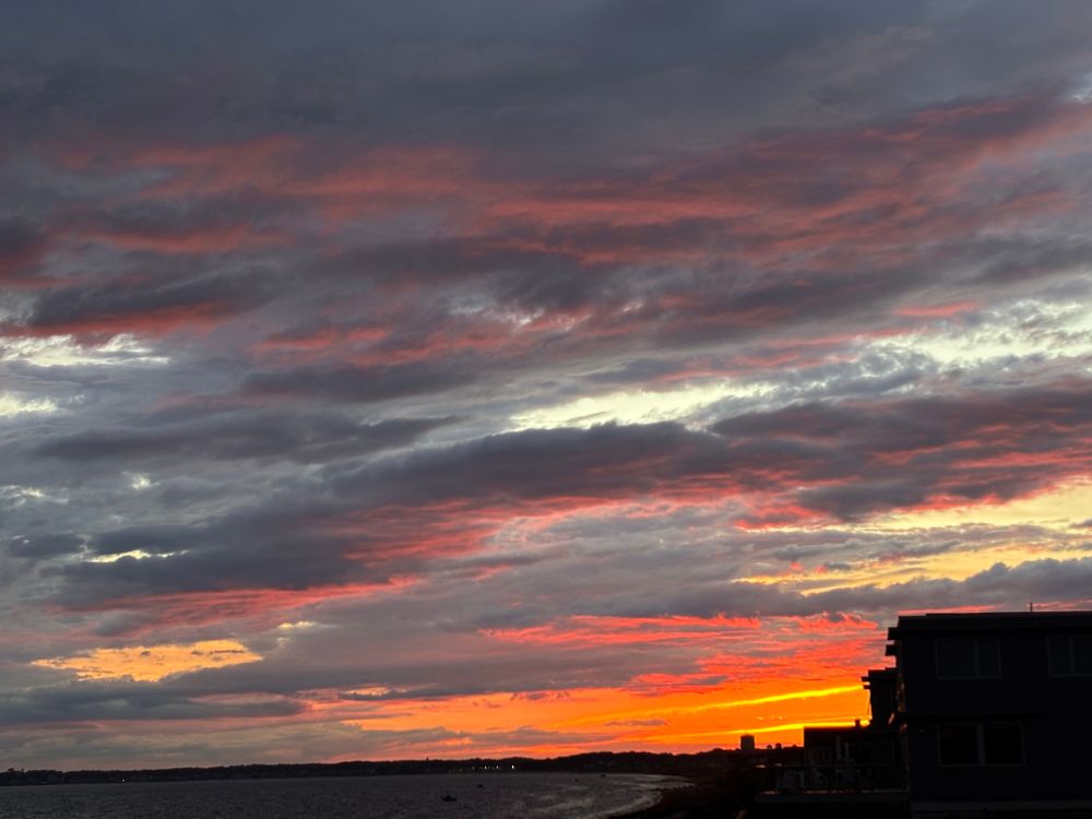 A sunset over Provincetown, MA, view from Truro, bay side. The orange is so bright. The cottages on the beach are in silhouette. 