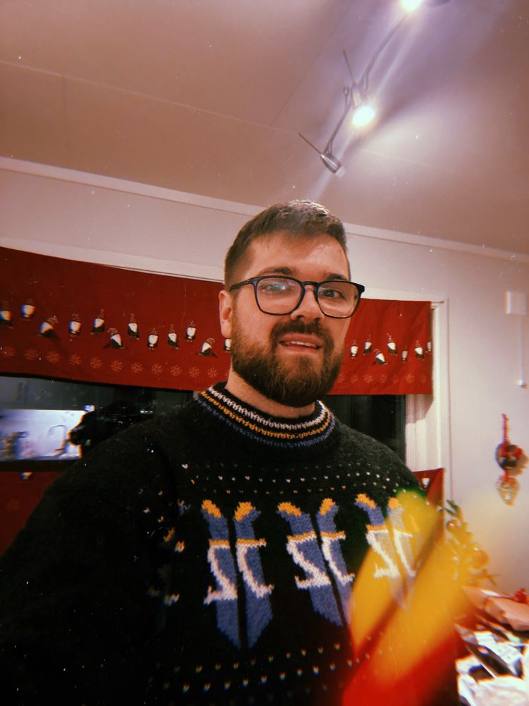 Eit bilete av meg med ein strikka genser med tre starcraft 2 logoar på. Eg smilar til kamera, har briller, brunt hår og skjegg. Bak meg heng det raude julegardiner.