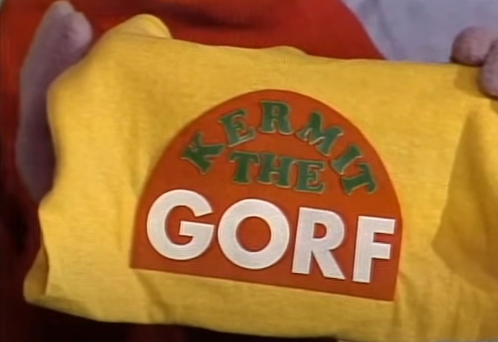 A Muppet holding up a t-shirt with the words 'Kermit the GORF' printed on it. 