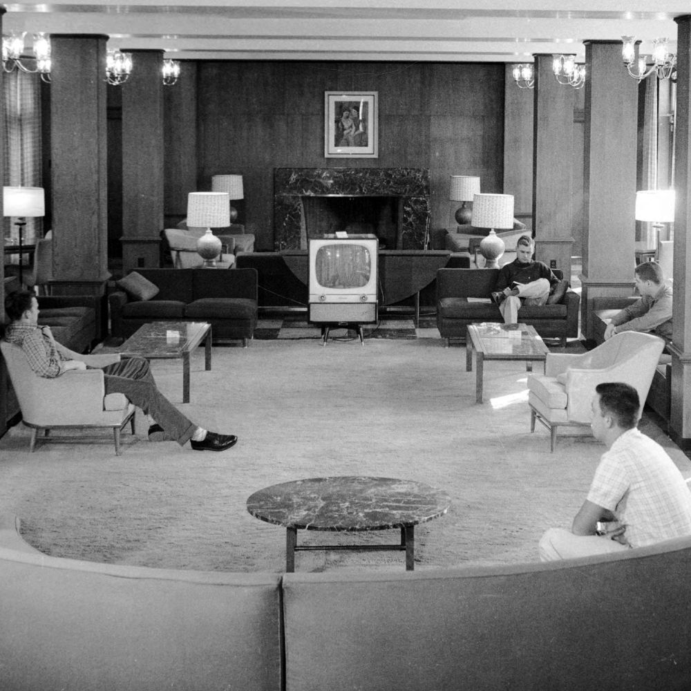 View of Washington Hall interior from behind a rounded couch. 4 people lounge on various pieces of furniture.