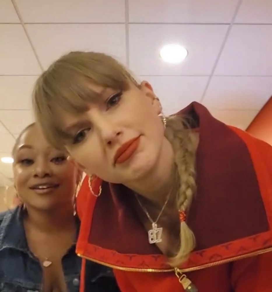 taylor swift looking into the camera confused with a friend standing behind her
