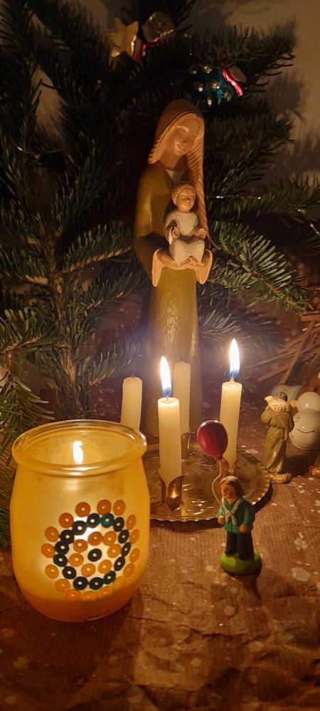 Un photophore contenant la Lumière de la paix de Bethléem avec un santon scout et une Vierge à l'enfant devant une crèche