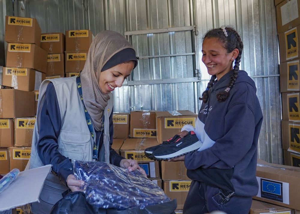An IRC staff person gives a Palestinian girl a winter kit. They are both smiling.
