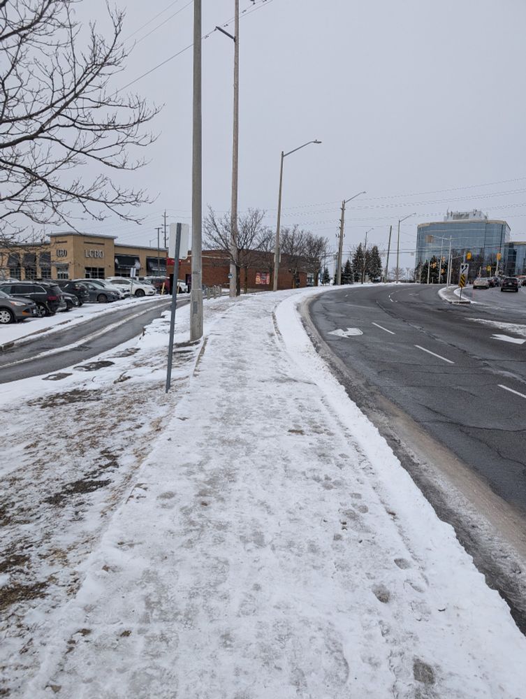 Image shows Ottawa street. The left hand side shows a clear lane for the Tim Horton's drive-through. To the right is a clear road to Gloucester Mall. In the centre is the sidewalk completely covered in ice and snow. No attempt has been made to clear it.