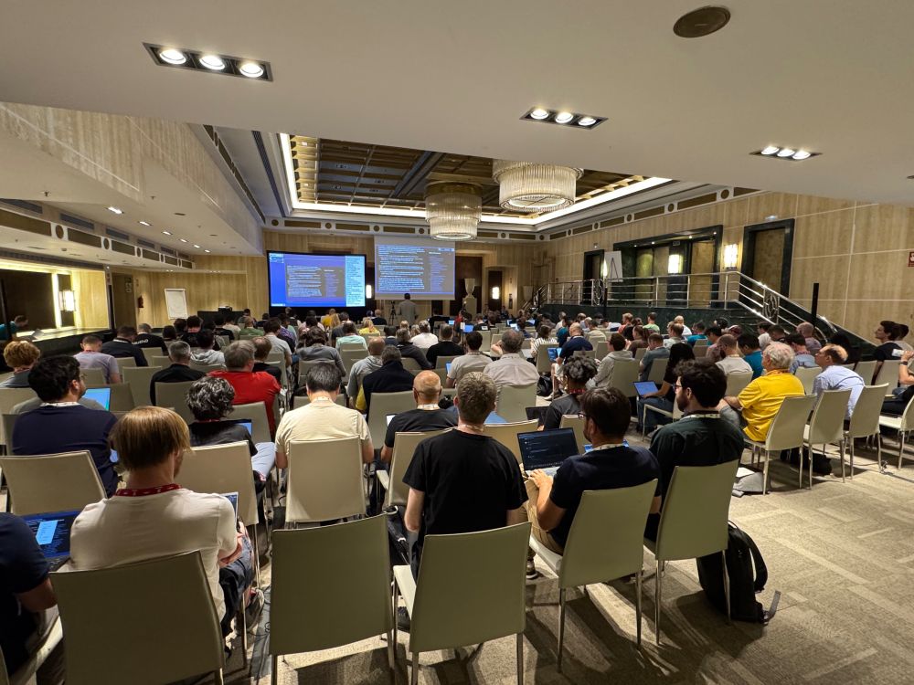 Audience members seated at the AI PREF working group session at the IETF 123 Madrid meeting viewing a large screen displaying slides, in a room with ornate ceiling and lighting.