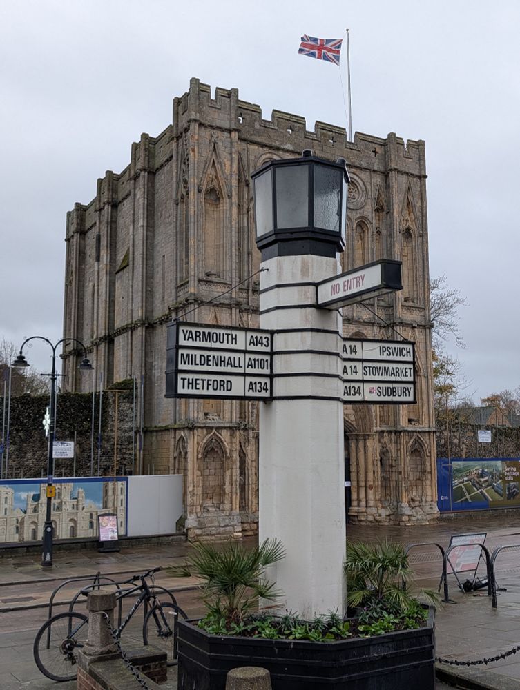 Finger post sign on thick white pillar with illuminated top beacon. Medieval abbey gatehouse to test.