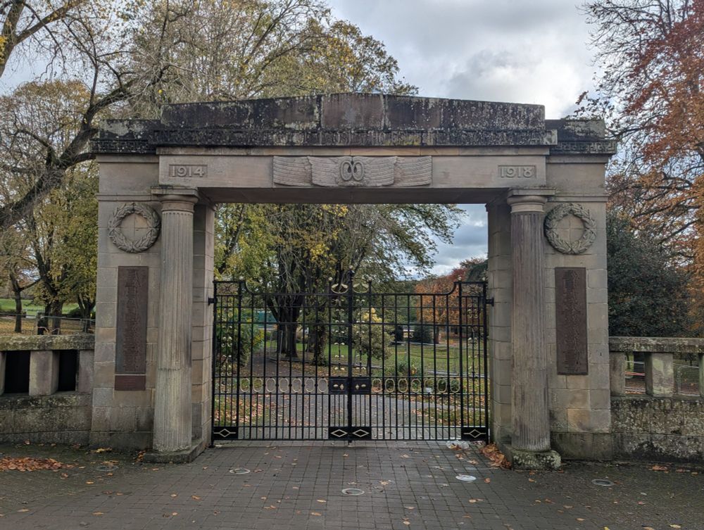 Grade II listing details: War Memorial Arch to Park. Stone arch with fluted pillars, main side balustrades and additional pillars with square caps and ball finials. Arch has bas relief carving and lettering. Iron double gates, part wrought, part cast, iron, with some gilding.
