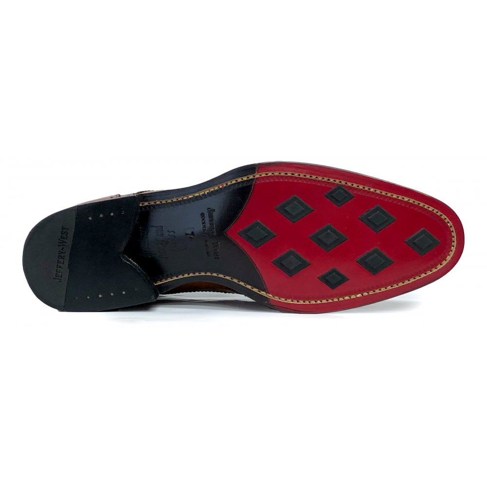 Bottom view of a black leather dress shoe with a red sole featuring black diamond-shaped rubber grip inserts. The heel is black with “Jeffery-West” stamped on it.