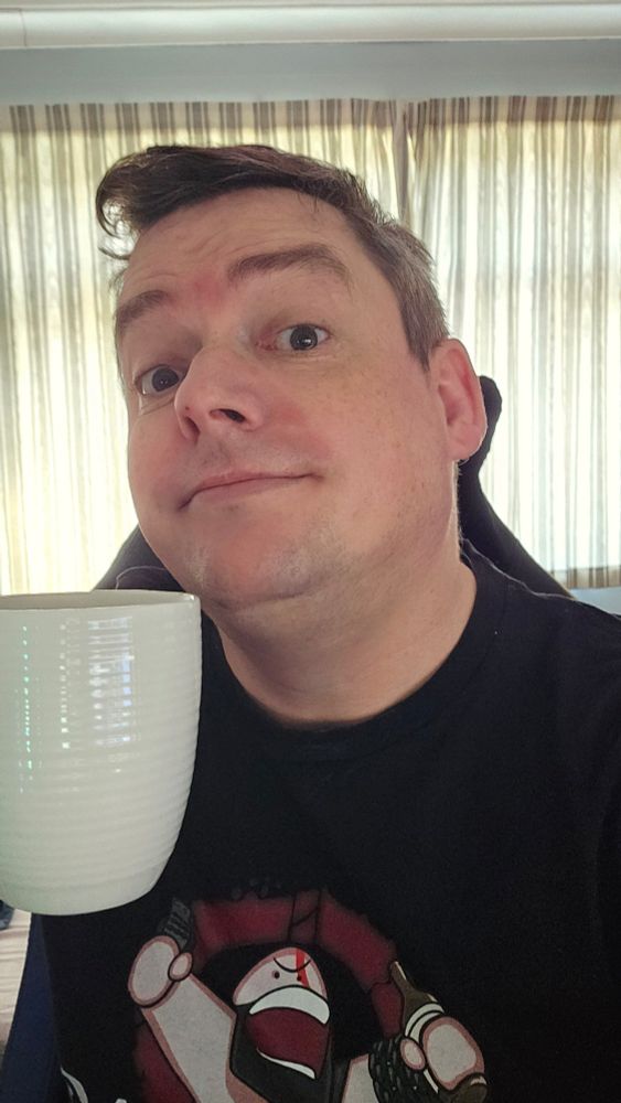 A guy holding up a cup of tea while half smiling, his head tilted back a little.