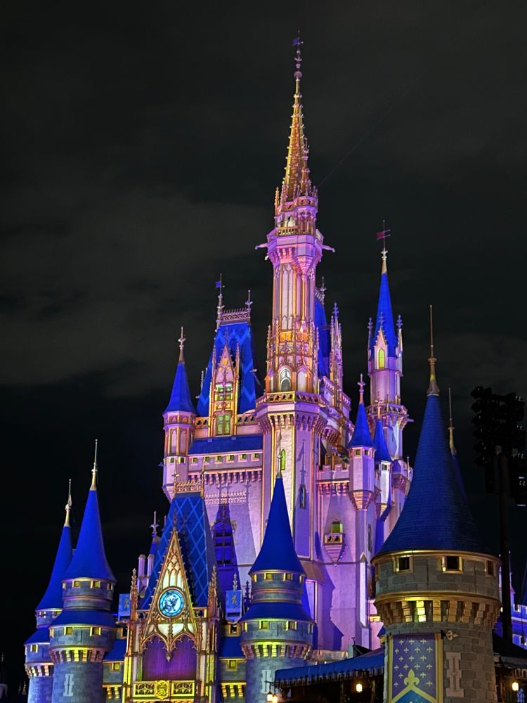 Cinderella castle at Walt Disney World. The upper turrets are lit in pink which pops against a cloudy dark gray night sky. 