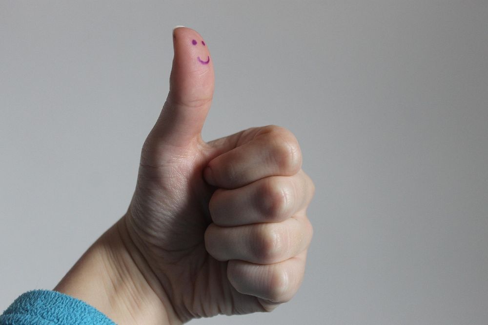 Hand giving thumbs up with a smiley on the thumb. 