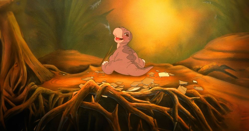 Still cell image from the land before time 1988 feature. Up close is a bunch of roots and pieces of eggshell over a small dirt hill with a stump. A tiny baby littlefoot is sitting backwards, but has his neck turned to face the 'camera' and is happily smiling with blushy cheeks. Littlefoot is a longneck and is purple-ish in color. The background has soft light painted in with green ferns and distant foilage
