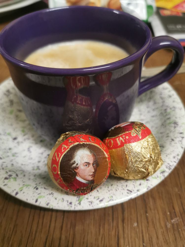 A cup of coffee and two Mozartkugeln in front of it. 