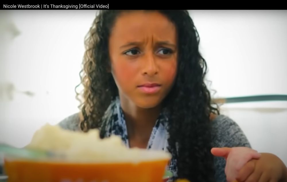 a very confused girl looks on as her friend raps a Thanksgiving prayer in the song "It's Thanksgiving" by Nicole Westbrook