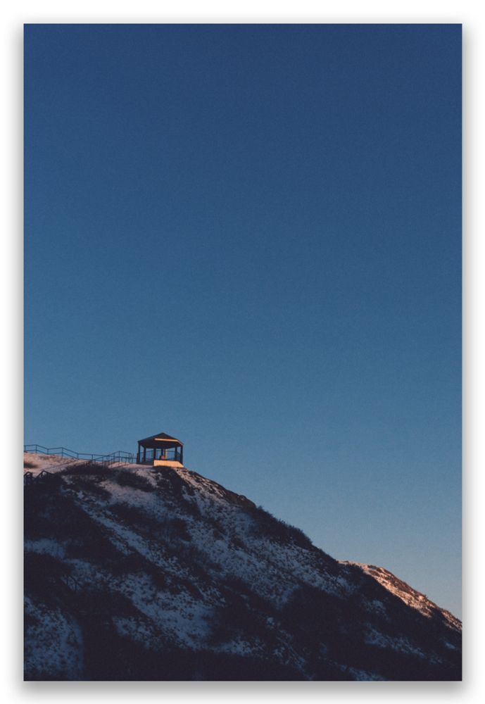 A photo of a gazebo baked in the last golden light of the sunset atop a hillside already lost to darkness