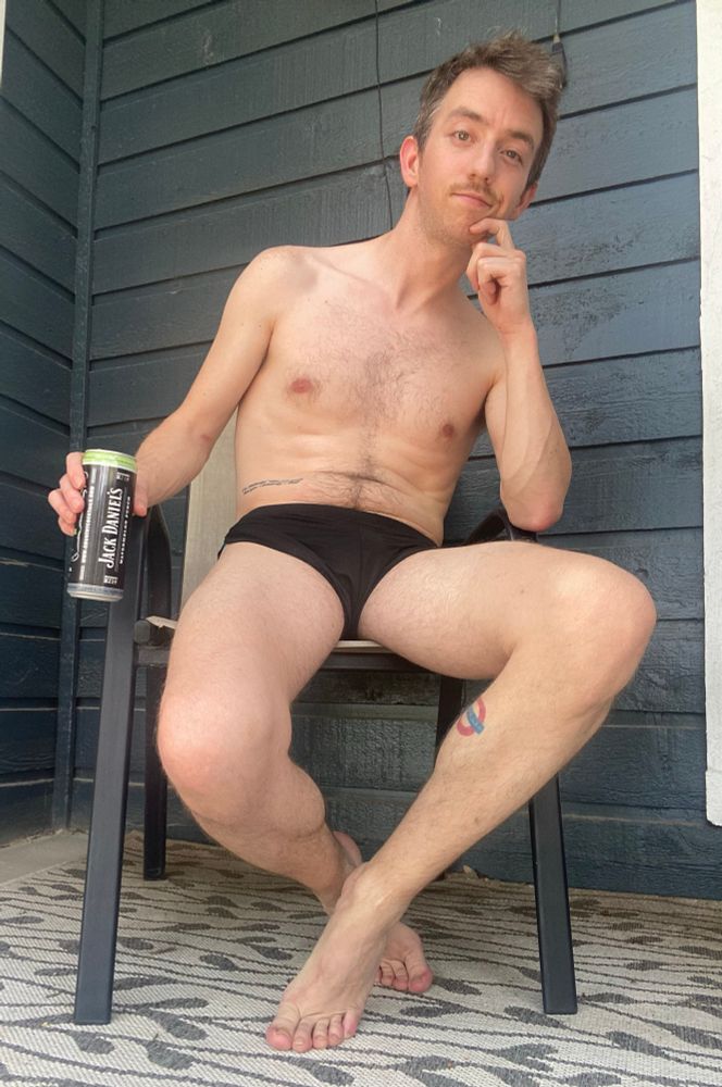 Shirtless and wearing slutty shorts on patio, holding a drink in my right hand, my left hand caressing my chin in a pensive manner