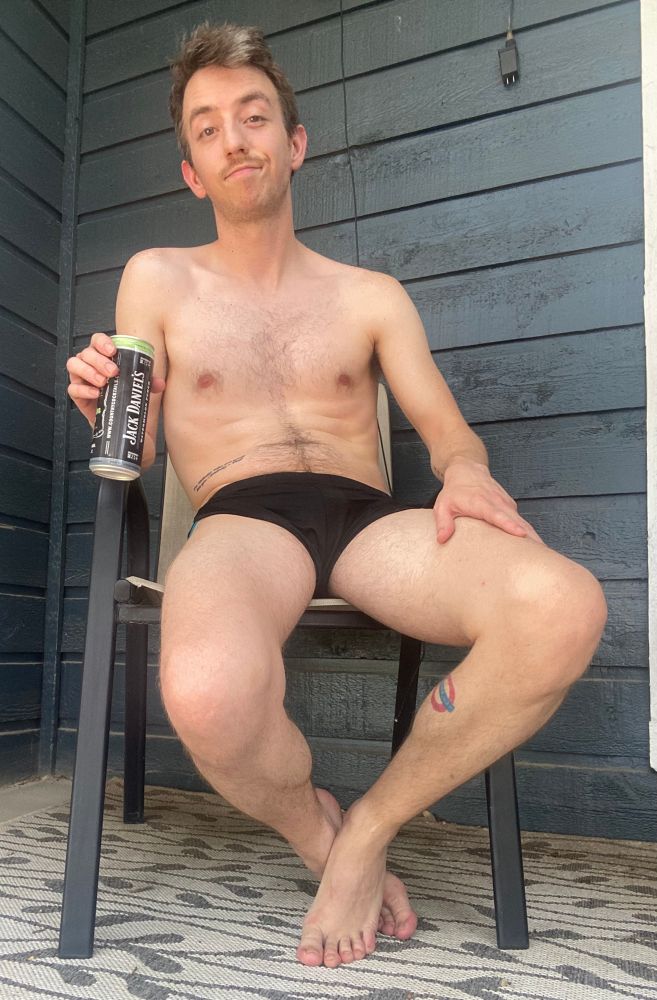 Shirtless and wearing slutty shorts on patio, holding a drink in my right hand, my left hand resting on my left thigh