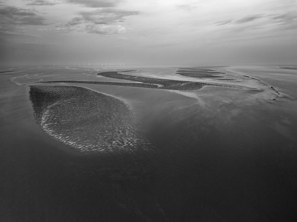 Aerial view of the River Mersey at low tide, with sand patterns and wind turbines in the distance.