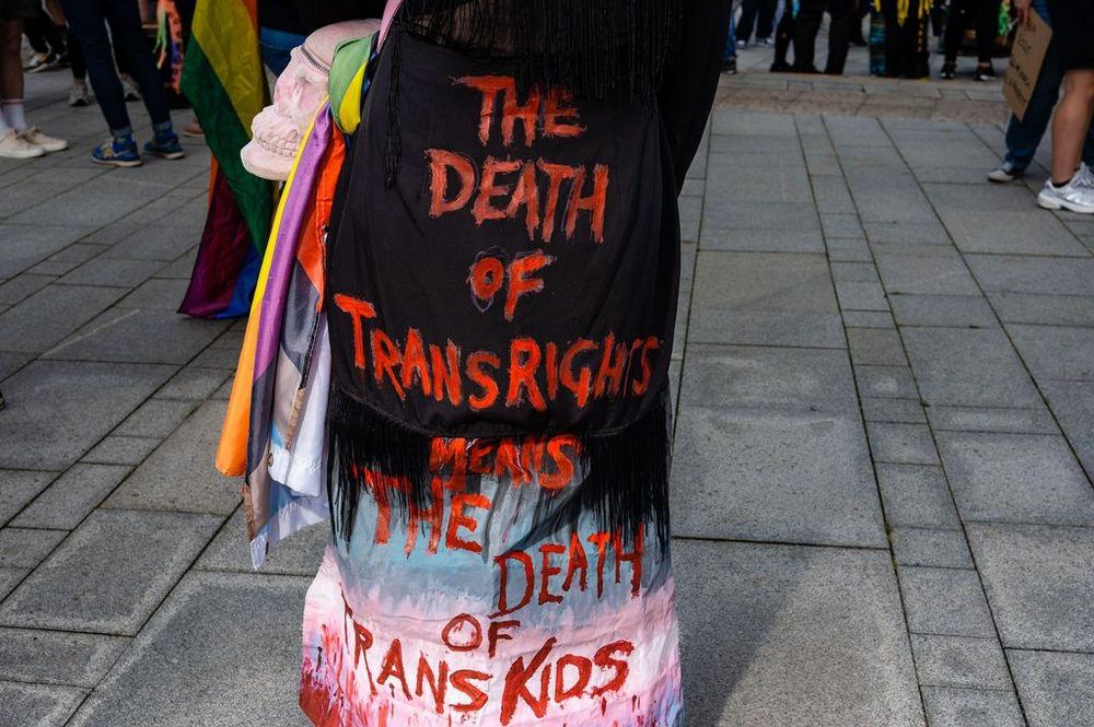 A person at Liverpool Pride wearing a black garment with the words 'The Death of Trans Rights Means The Death of Trans Kids' written in red.