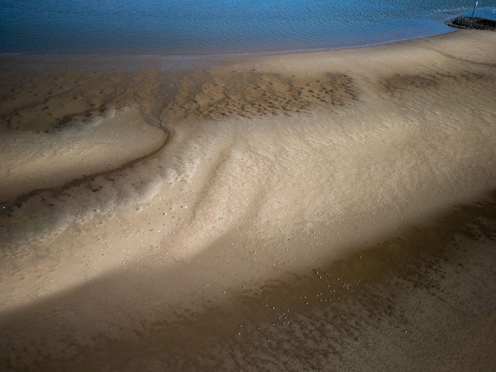 Aerial drone shot of a sandy beach with water, taken in New Brighton, UK.