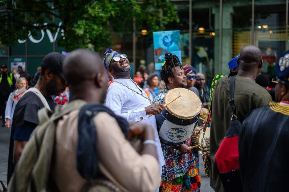 People marching in a parade, with some playing drums and wearing colorful clothing.