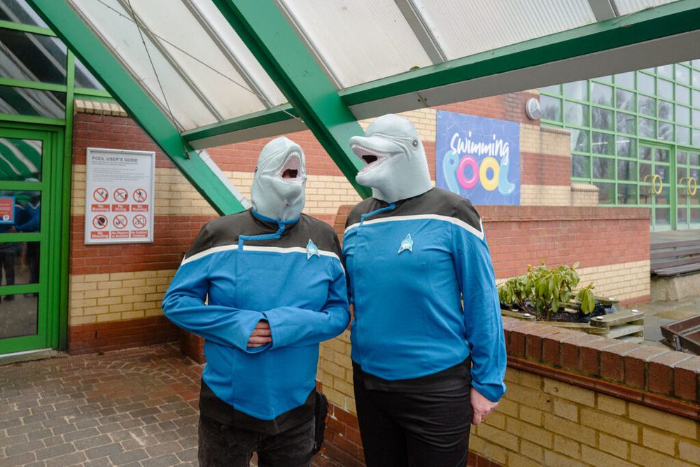 Two people dressed in Star Trek uniforms and dolphin masks stand outside a swimming pool.