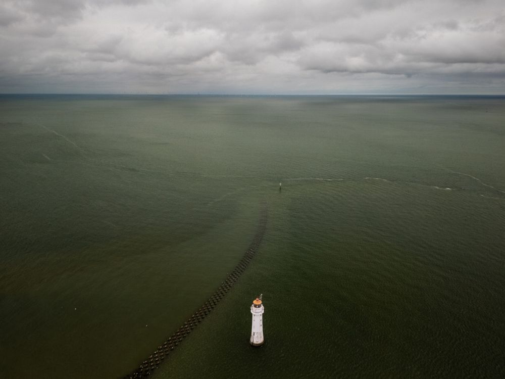 An aerial view of New Brighton Lighthouse in the Irish Sea with a cloudy sky.