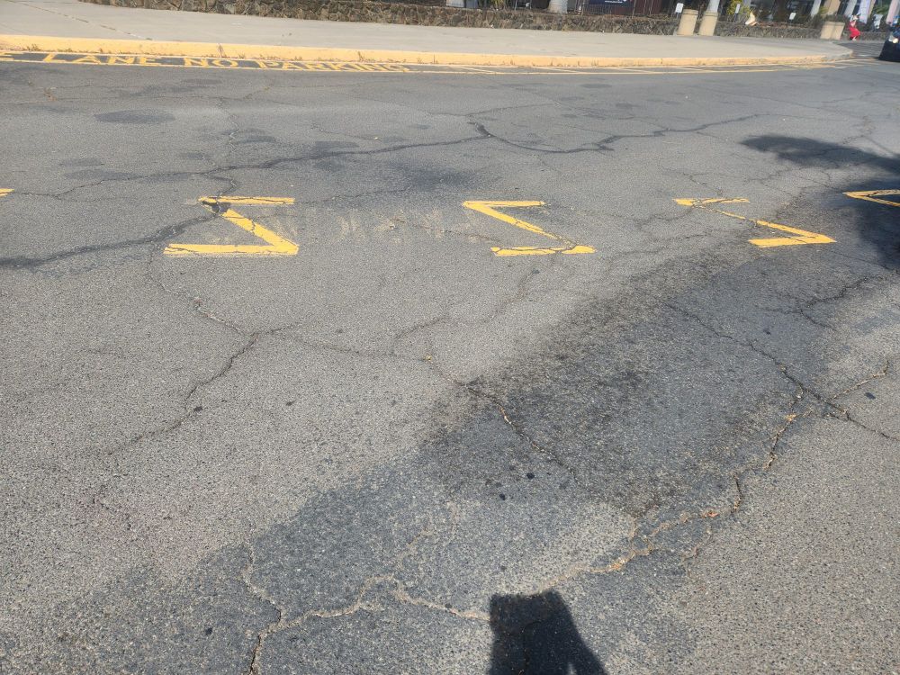 Picture of a parking lot road with yellow markers for a fire lane shaped like multiple Zs