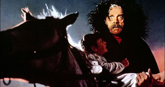 Boris Karloff as Gorca in Black Sabbath on horseback, carrying a small child, wide-eyed, wearing a hooded cloak