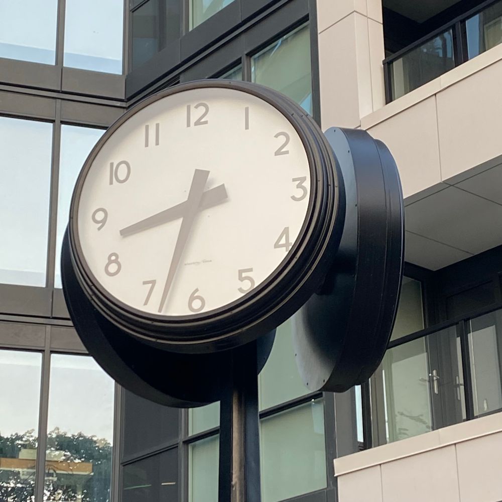 A round clock on a pole  in an outdoor courtyard showing the time 8:33.