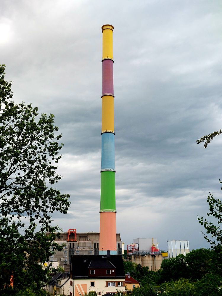 In der Mitte des Bildes steht ein hoher Schornstein vor grauem Wolkenhimmel.
Im unteren Teil sind die Gebäude eines Heizkraftwerkes zu sehen.
Der Schornstein ist in 6 Segmente geteilt, von denen jedes in einer anderen Farbe gestrichen wurde.
Von oben: Gelb, Violett, Dunkelgelb, Blau, Grün, Orange.
