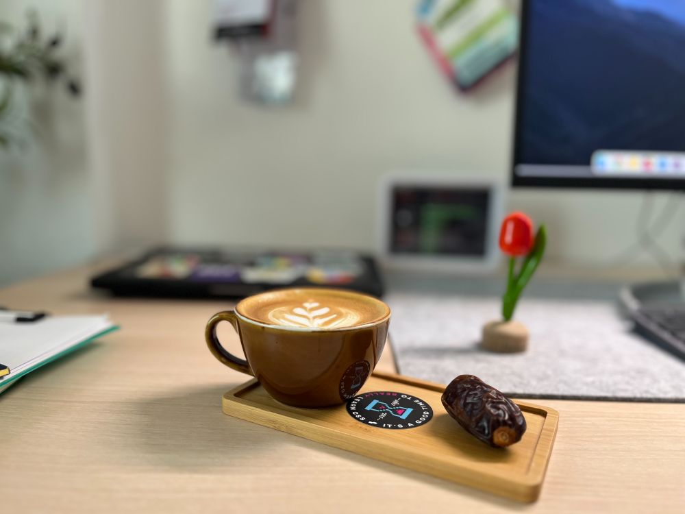 Latte in a brown cup with a date and a CSS Café sticker on a wooden tray.