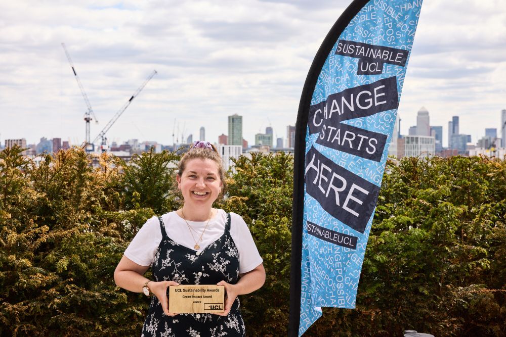 Our colleague Amy-Laura holding the IOE Library's Green Impact gold award in front of the London city skyline.