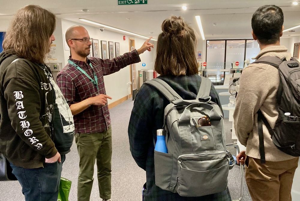 A friendly IOE librarian speaks to a group of students standing in front of him in the IOE Library.