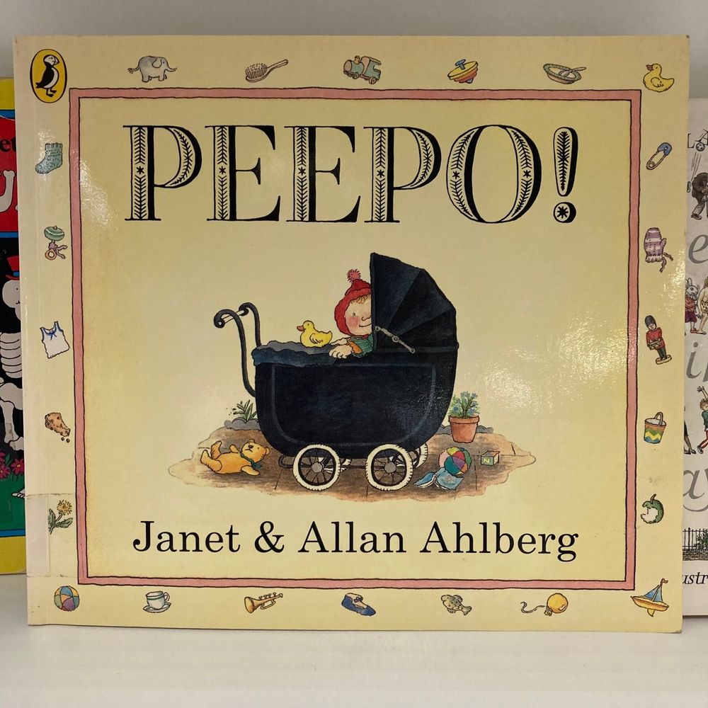 The front cover of Peepo! by Janet and Allan Ahlberg on a library shelf.
