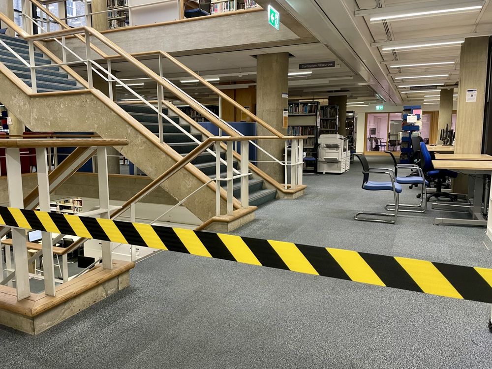 Library staircase. Yellow and black hazard tape cuts across the image. 