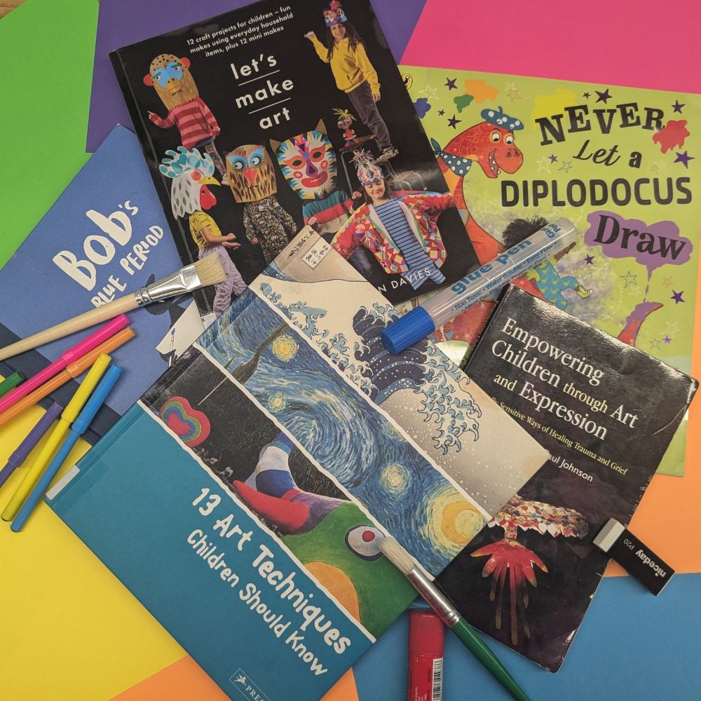 Five books set against brightly coloured paper, with a handful of coloured markers, glue sticks, and paintbrushes scattered around. The books are titled "Bob's Blue Period," "Let's Make Art," "Never let a Diplodocus Draw," "13 Art Techniques Children Should Know," and "Empowering Children through Art and Expression."