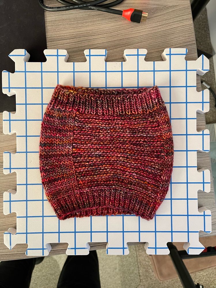 A multicolor knit cowl on a blocking mat after being blocked showing that the cowl has grown lengthwise by at least an inch